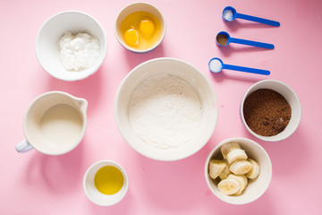 Visual guide made of single photo showing the different step to prepare a banana bread, ingredients to prepare the bread , eggs, flour, sugar, grreek yogurt, oi and butter, and banana,are displayed ov