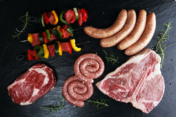 Assorted delicious raw meat with vegetable on a barbecue with t-bone steak, sausages and meat...