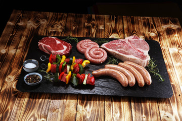 Assorted delicious raw meat with vegetable on a barbecue with t-bone steak, sausages and meat...