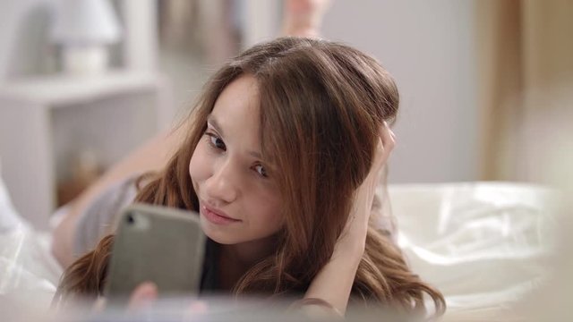 Model girl taking selfie photo in bed. Happy woman taking photo on mobile phone