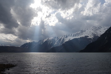 Sun rays breaking through clouds, sunlight on lake, snowy mountains behind lake