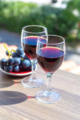 Two wine glasses with red wine served with red grape on outdoor terrace