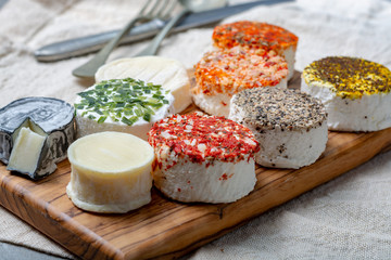Assortment of French fresh white soft goat cheeses with different tastes topping made with herbs, paprika, indian curry, bruscetta, chives and dried tomatoes