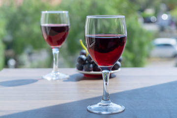 Two wine glasses with red wine served with red grape on outdoor terrace