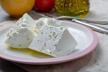 Fresh young soft white Feta cheese with olive oil on plate seasoned with dried oregano herb