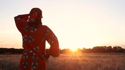 HD Video clip of African woman in traditional clothes standing in a field of crops looking to the sun at sunset or sunrise