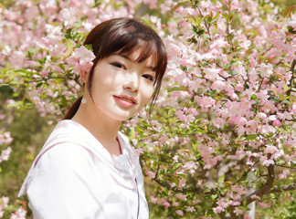 Outdoor portrait of beautiful young Chinese girl smiling among blossom cherry tree brunch in spring garden, beauty, summer, emotion, expression and people lifestyle concept.