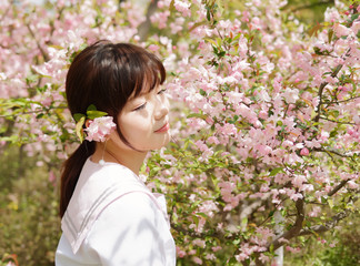 Outdoor portrait of beautiful young Chinese girl smiling among blossom cherry tree brunch in spring garden, beauty, summer, emotion, expression and people lifestyle concept.