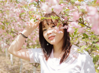 Outdoor portrait of beautiful young Chinese girl smiling among blossom cherry tree brunch in spring garden, beauty, summer, emotion, expression and people lifestyle concept.