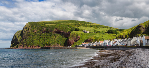 Stone beach and row of white houses of Pennan coastal fishing village on North Sea in Aberdeenshire Scotland UK with Black Hill sea cliff