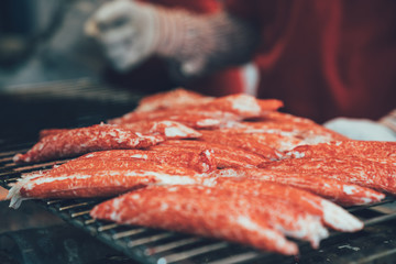 Delicious grilled crab legs street food at Kuromon Ichiba Market Osaka japan. japanese fresh seafood in vendor cooking hot tasty on iron plate indoor place with unrecorgnized hands in gloves.