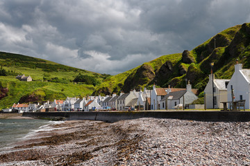 Stone beach and row of white houses of Pennan coastal fishing village on North Sea in Aberdeenshire Scotland UK with green sea cliffs
