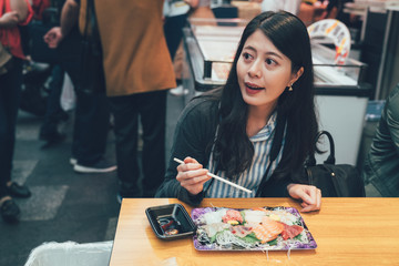 Fototapeta premium vintage picture of young local woman dining at tradition japanese food restaurant vendor in kuromon ichiba market osaka japan. elegant lady sitting in teeming street enjoy lunch fresh seafood sashimi