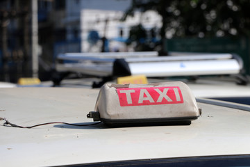 Broken taxi light sign or cab sign in drab white and red color with white text on the car roof at the street.