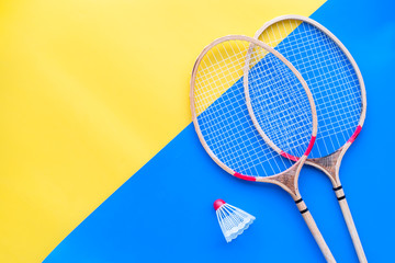 Badminton equipment. Badminton rackets and shuttlecock on yellow and blue background top view copy space