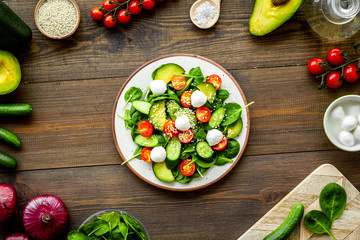 Cooking fresh salad. Vegetables, greens, spices, plate of salad on dark wooden kitchen desk top view