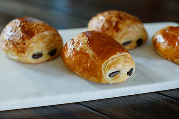 French Chocolate Croissants Fresh From the Oven Served on a White Marble Cutting board on a Rustic Wood Table