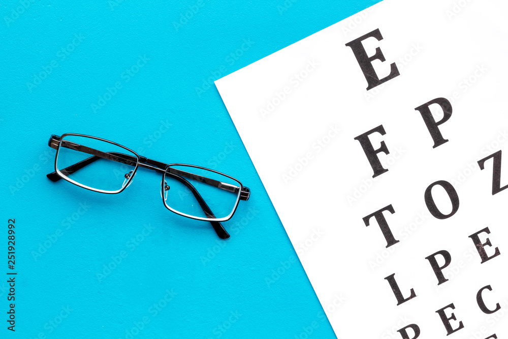 Wall mural eye examination. eyesight test chart and glasses on blue background top view