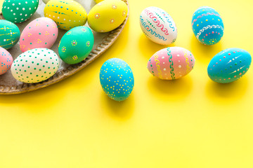 Easter traditions. Colorful Easter eggs in basket on yellow background top view copy space