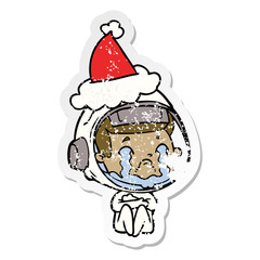 distressed sticker cartoon of a crying astronaut wearing santa hat