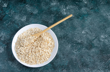 oatmeal in white plate on blue background and wooden spoon