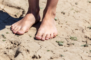 Fototapeta na wymiar Girl's bare feet on dry ground