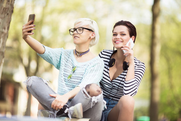 Young students sitting outdoors and using smartphones