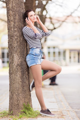 Young student leaning on a tree and listening to a music outdoors