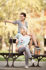 Young beautiful students sitting on a bench outdoors and taking a photos
