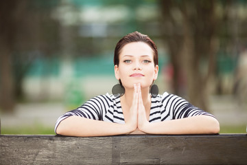 Young woman sitting on a bench outdoors and looking in to a camera