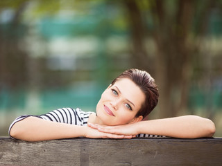Beautiful young woman sitting on a bench outdoors and looking in to a camera