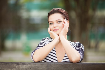 Beautiful happy woman sitting on a bench outdoors and looking in to a camera