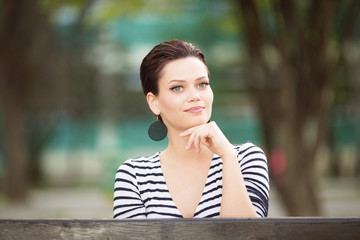 Beautiful young woman sitting on a bench outdoors and looking in to a objective