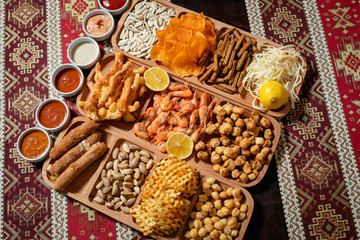 Set of beer snacks, eleven varieties and six sauces on a wooden table with a tablecloth with national patterns