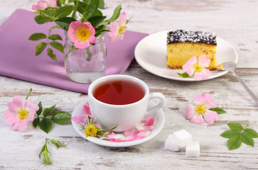 Obraz na płótnie Canvas Cup of tea with cheesecake and wild rose flower on rustic board