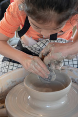 Asian kid working engraved pattern on terra cotta dish.