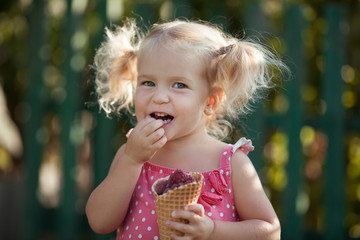 Naklejka premium Happy little girl is eating berries in summer garden, outdoor.