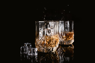 Two glasses of whiskey with ice cubes served on dark background