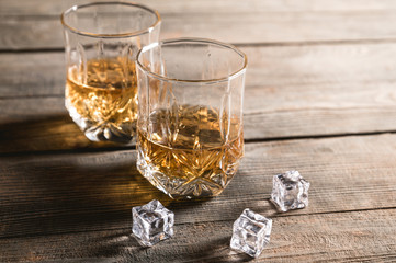 Two glasses of whiskey with ice cubes served on wooden planks 