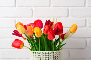 tulip flowers are in a basket on the table, white brick wall as background