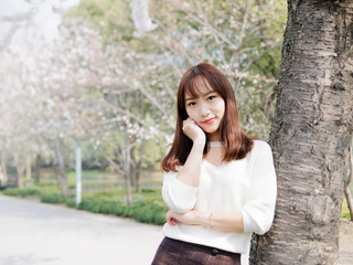 Outdoor portrait of beautiful young Chinese girl smiling among blossom cherry tree brunch in spring garden, beauty, summer, emotion, expression and people lifestyle concept.