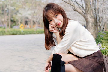 Outdoor portrait of beautiful young Chinese girl sitting and smiling among blossom cherry tree brunch in spring garden, beauty, summer, emotion, expression and people concept. 