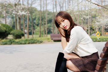 Outdoor portrait of beautiful young Chinese girl sitting and smiling among blossom cherry tree brunch in spring garden, beauty, summer, emotion, expression and people concept. 