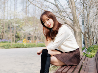 Outdoor portrait of beautiful young Chinese girl sitting and smiling among blossom cherry tree brunch in spring garden, beauty, summer, emotion, expression and people concept. 
