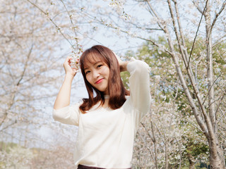 Outdoor portrait of beautiful young Chinese girl smiling among blossom cherry tree brunch in spring garden, beauty, summer, emotion, expression and people lifestyle concept.
