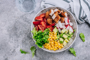 Healthy lunch bowl. Avocado, chicken, tomato, radish, corn, green leaves vegetables salad. Concrete background. Top view. Copy space