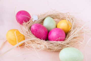pink, green, yellow Easter eggs in nest on beige background,