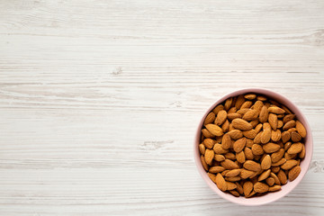 Full pink bowl of almonds over white wooden surface, top view. Overhead, flat lay, from above. Copy space.