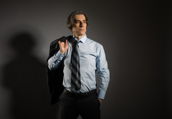 Naklejka premium An adult businessman in a shirt and tie looks confidently into the distance, holding a jacket in his hand behind his back.
