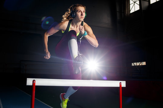 Young sportswoman running and jumping over hurdle